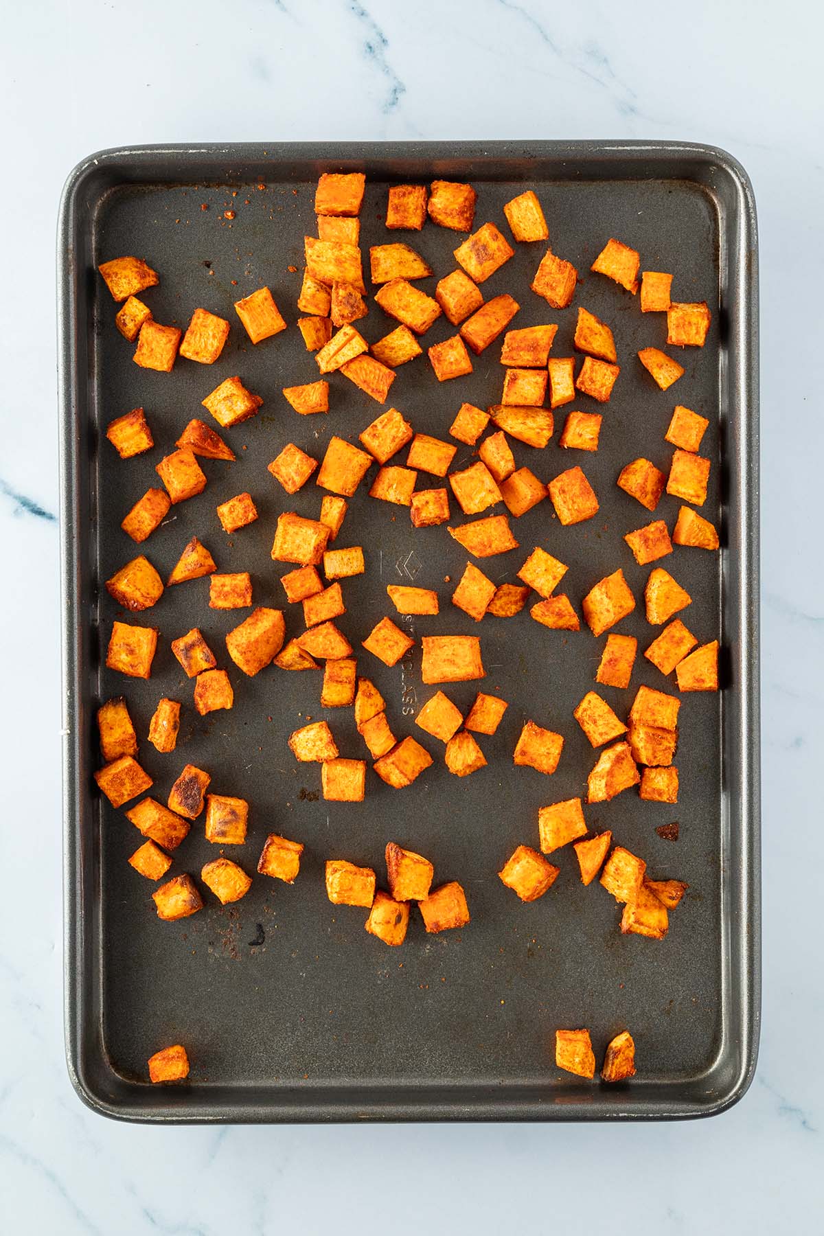 Knusprig ger&ouml;stete S&uuml;&szlig;kartoffelw&uuml;rfel auf einem Blech.