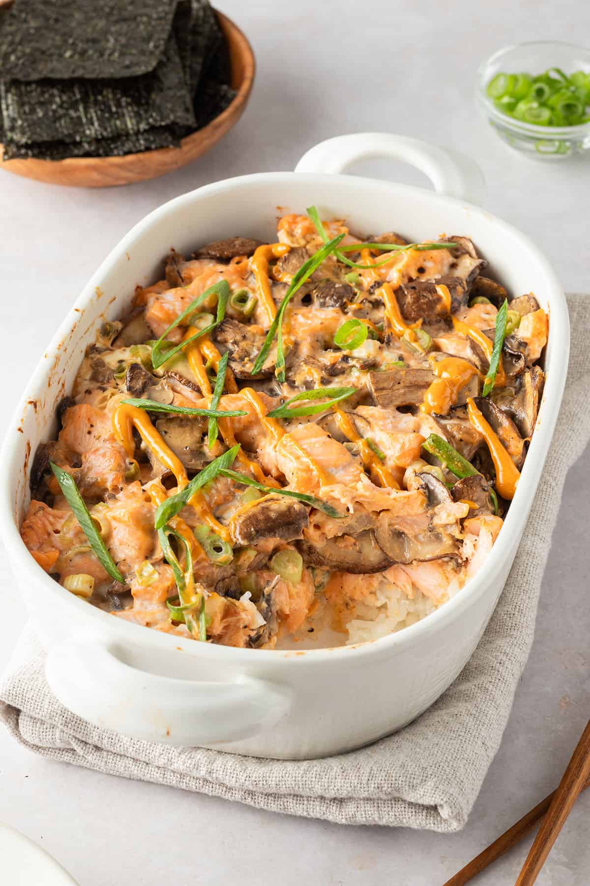 Sushi Auflauf in einer Auflaufform, Nori-Bl&auml;tter und Fr&uuml;hlingszwiebeln im Hintergrund.