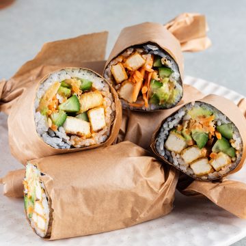 Mehrere, halbierte und in Papier eingewickelte Sushi Burritos mit Tofu auf einem Teller.