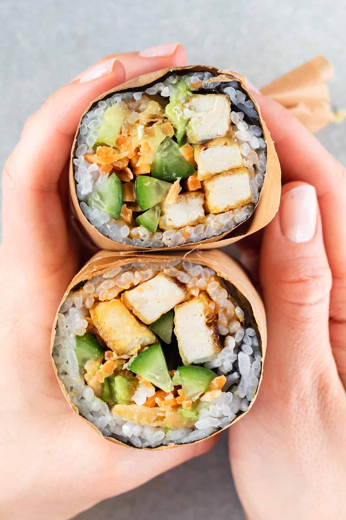 Zwei H&auml;nde halten einen halbierten Sushi Wrap in der Hand.