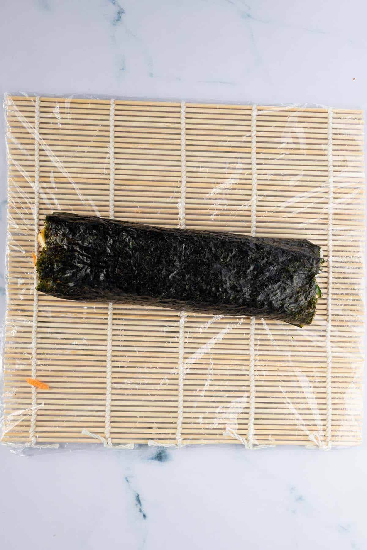 Eine ganze, dick gef&uuml;llte Sushi Rolle auf einer Bambus Matte.
