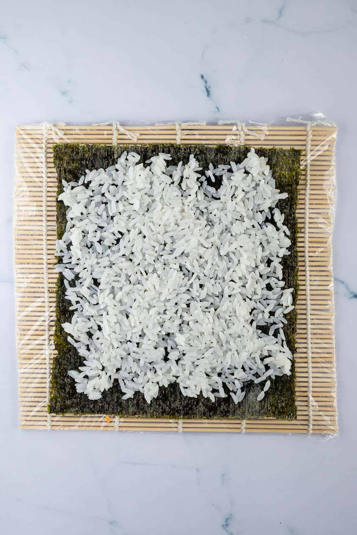 Sushi Reis wurde auf einem Nori Blatt verteilt, das auf einer Bambus Matte liegt.