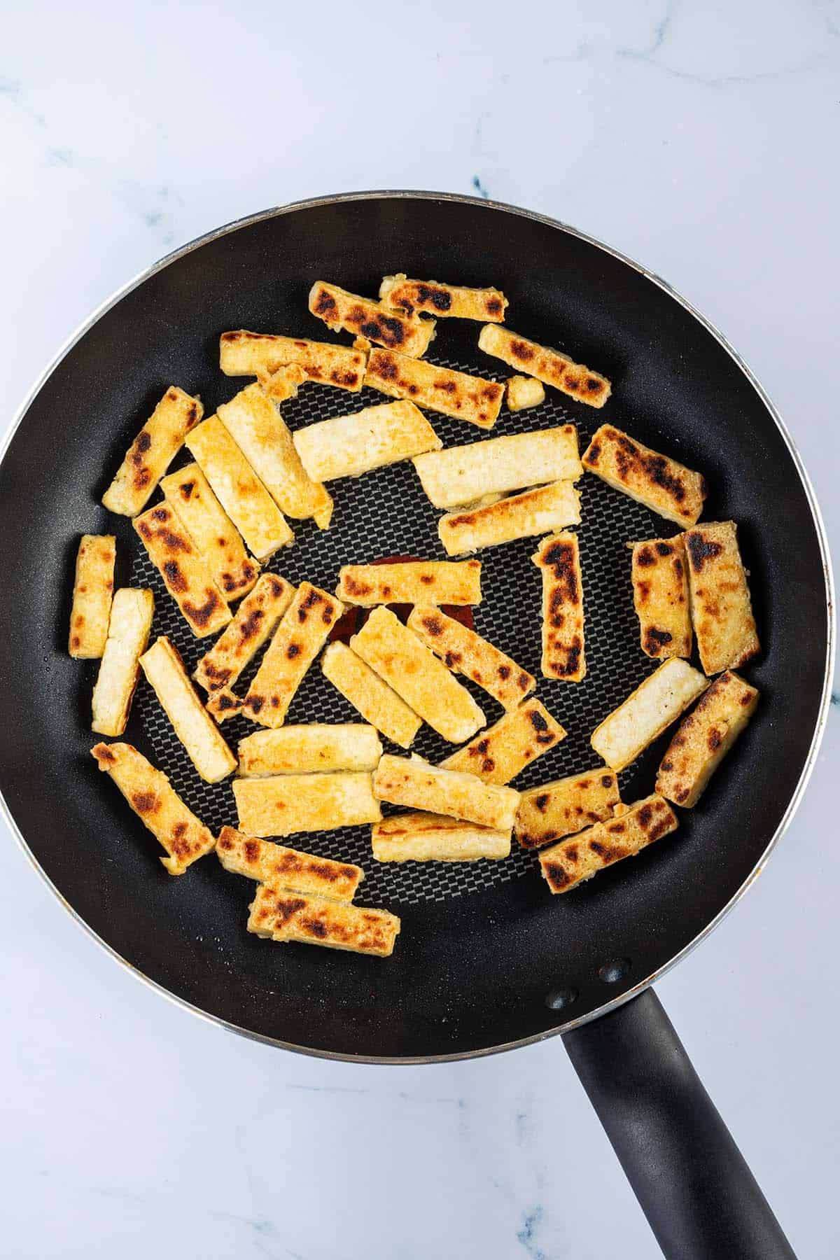 Knusprig angebratene Tofu Streifen in einer Pfanne.
