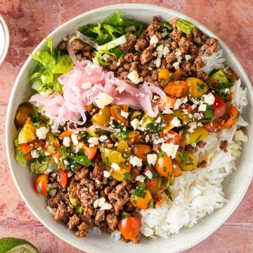 Taco Bowl mit Hackfleisch, Salsa, Reis und Salat auf einem roten Flie&szlig;enuntergrund, Deko im Bildrand.