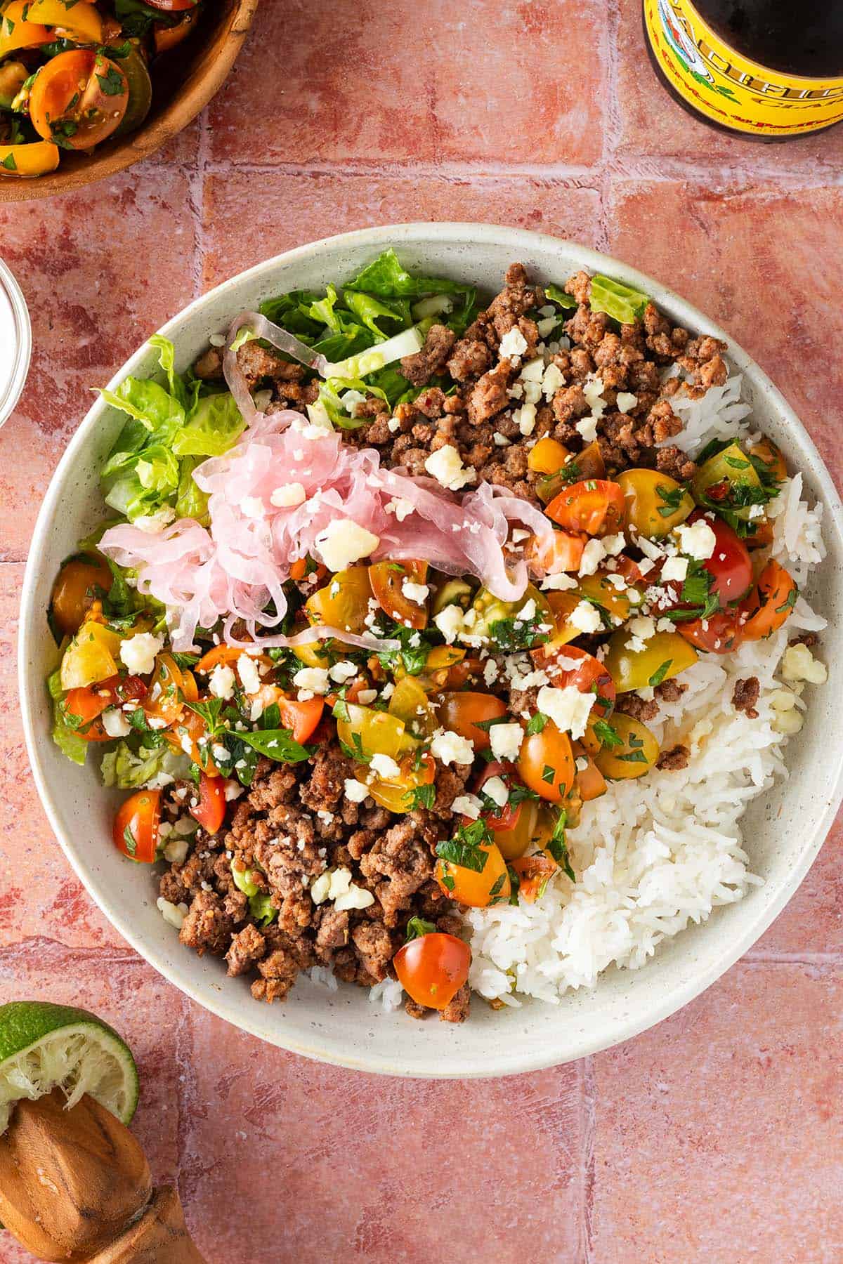 Taco Bowl mit Hackfleisch, Salsa, Reis und Salat auf einem roten Flie&szlig;enuntergrund, Deko im Bildrand.