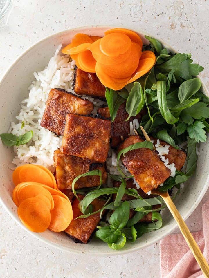 Tempeh Bowl mit frischen Kr&auml;utern, Reis, Karotten und knusprigen Erdnuss-Tempeh.