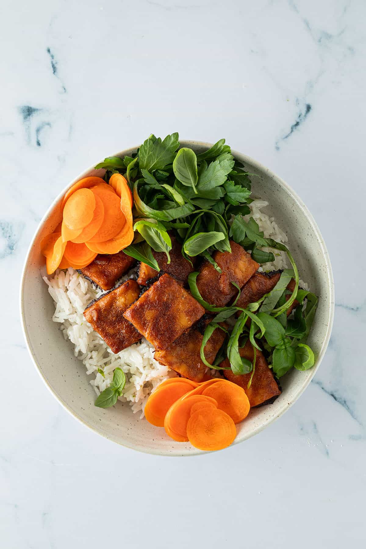 Reis, frische Kr&auml;uter, eingelegte Karotten und knusprig gebackener Tempeh in einer Bowl angerichtet.