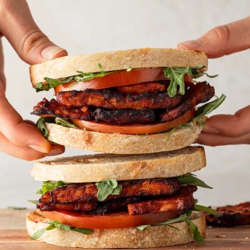 Jemand nimmt eines von zwei &uuml;bereinander gestapelten Tempeh Sandwiches weg.
