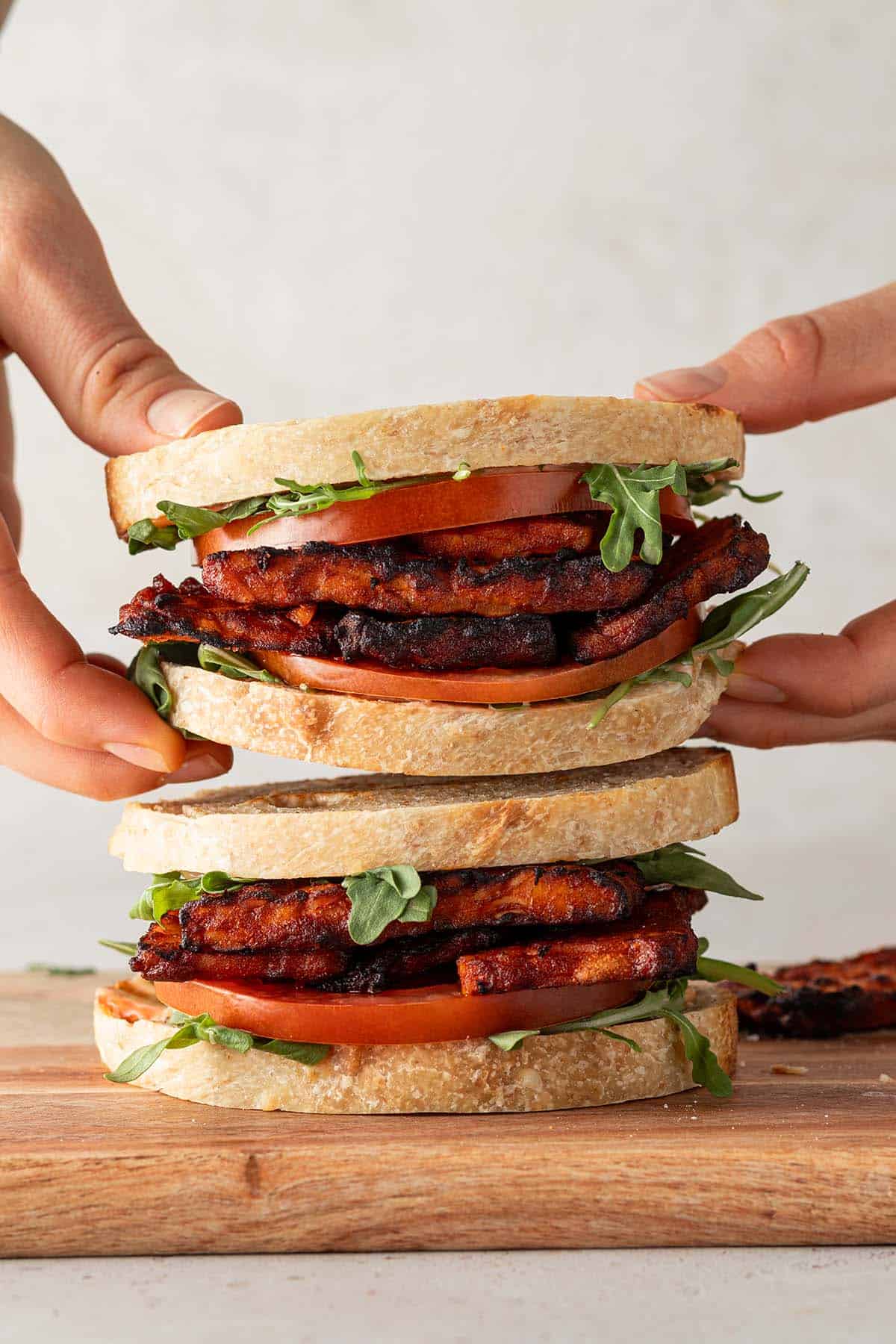 Jemand nimmt eines von zwei &uuml;bereinander gestapelten Tempeh Sandwiches weg.