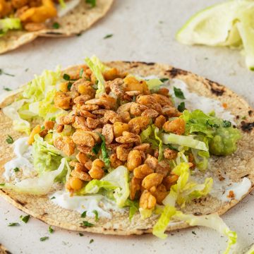 Veganer Taco mit knusprigen Tempeh und Salat, Limetten und weitere Tacos im Bildrand.
