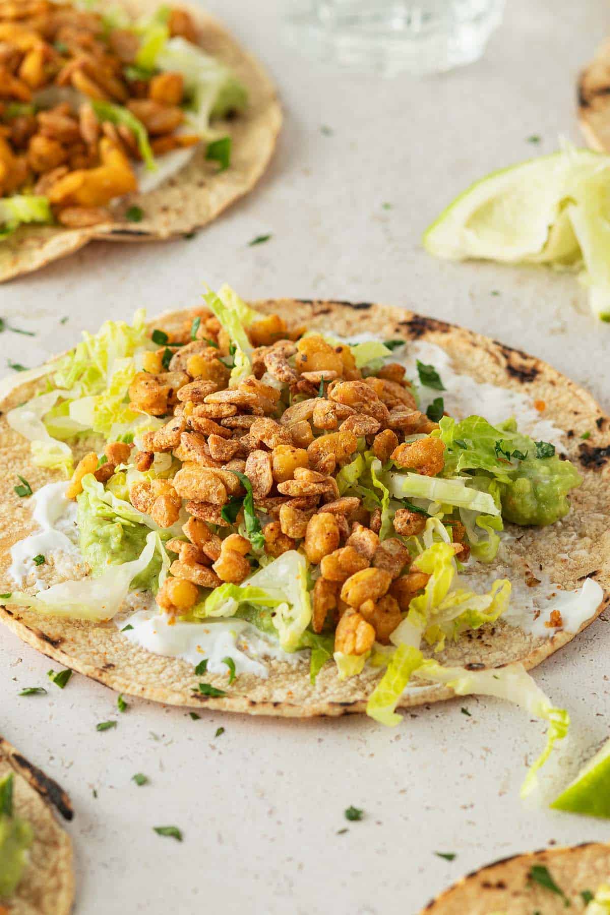 Veganer Taco mit knusprigen Tempeh und Salat, Limetten und weitere Tacos im Bildrand.