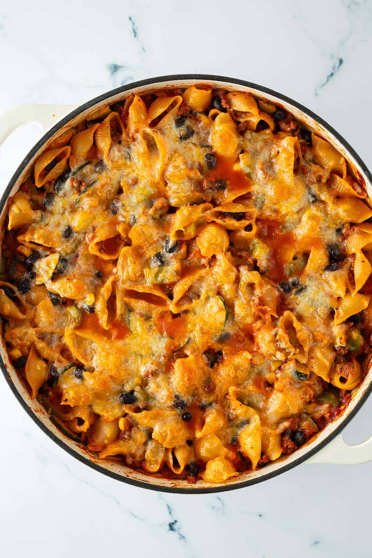Nahaufnahme eines frisch &uuml;berbackenen Nudelauflaufs mit geschmolzenem K&auml;se, Bohnen und Pasta in einer hellen Auflaufform.