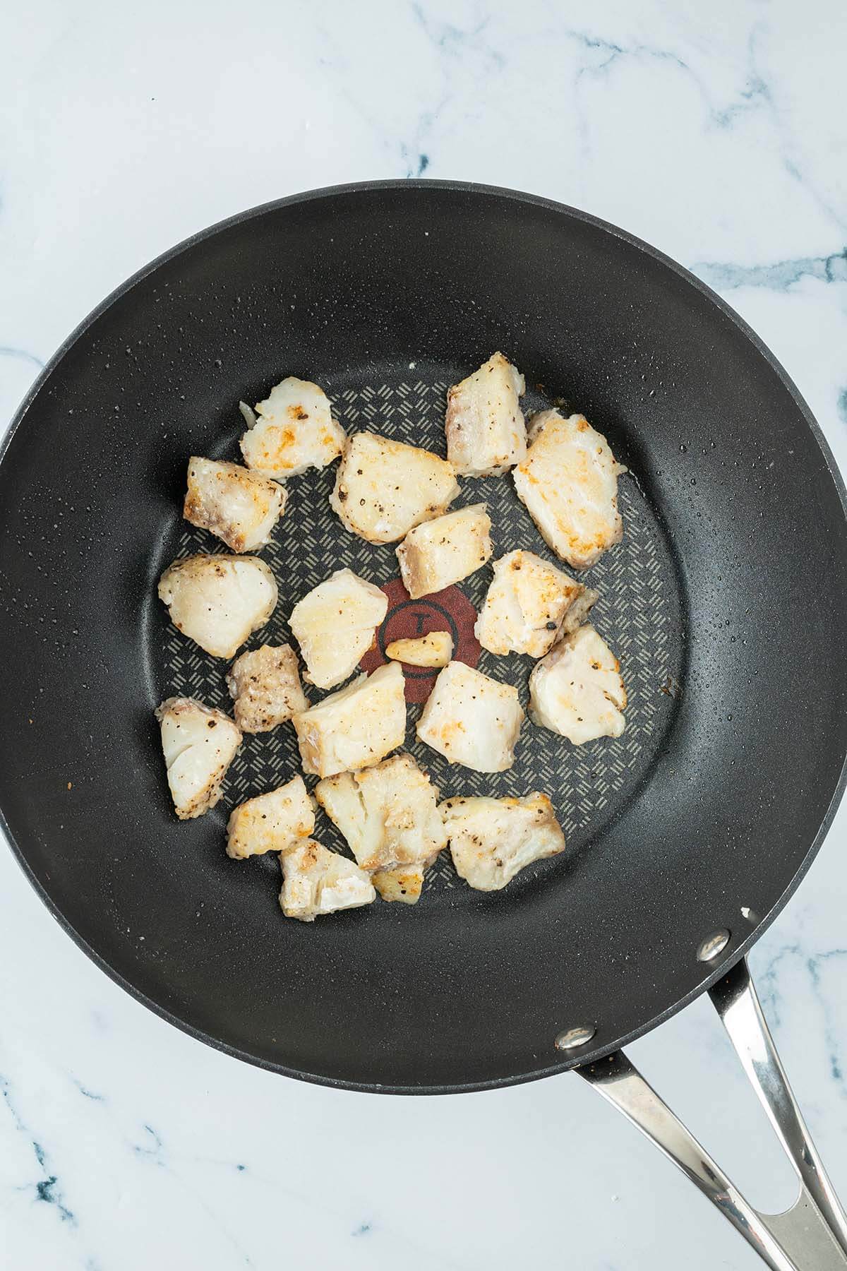 Angebratene wei&szlig;e Fischfiletst&uuml;cke in einem Wok.