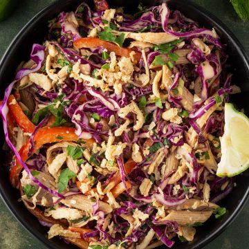 Thai Crunch Salat mit Erdnussdressing in einer schwarzen Sch&uuml;ssel auf dunkelgr&uuml;nem Untergrund, Deko im Bildrand.