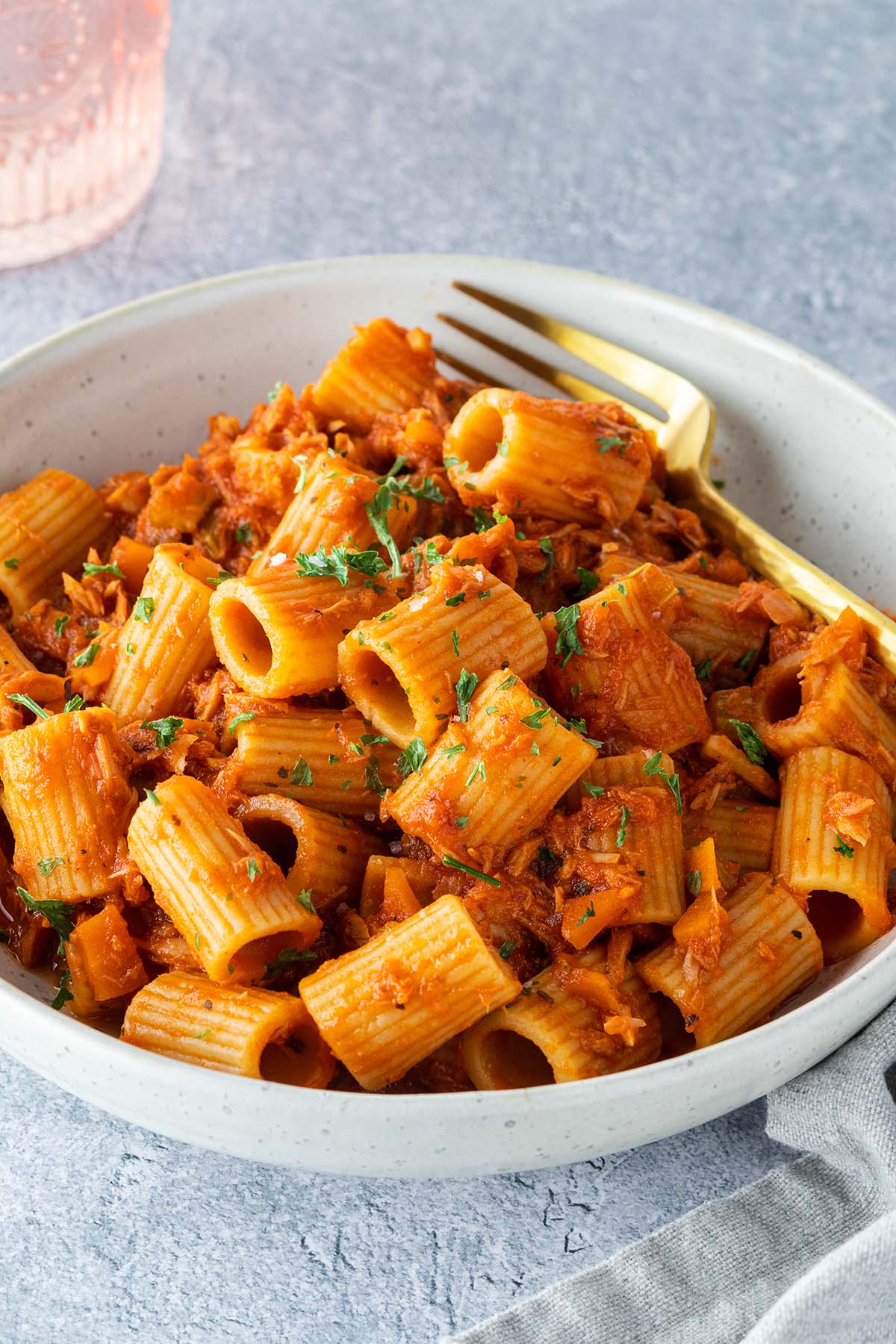 Ein Teller mit Rigatoni in einer Thunfisch-Toamtenso&szlig;e auf einem hellgrauen Untergrund.