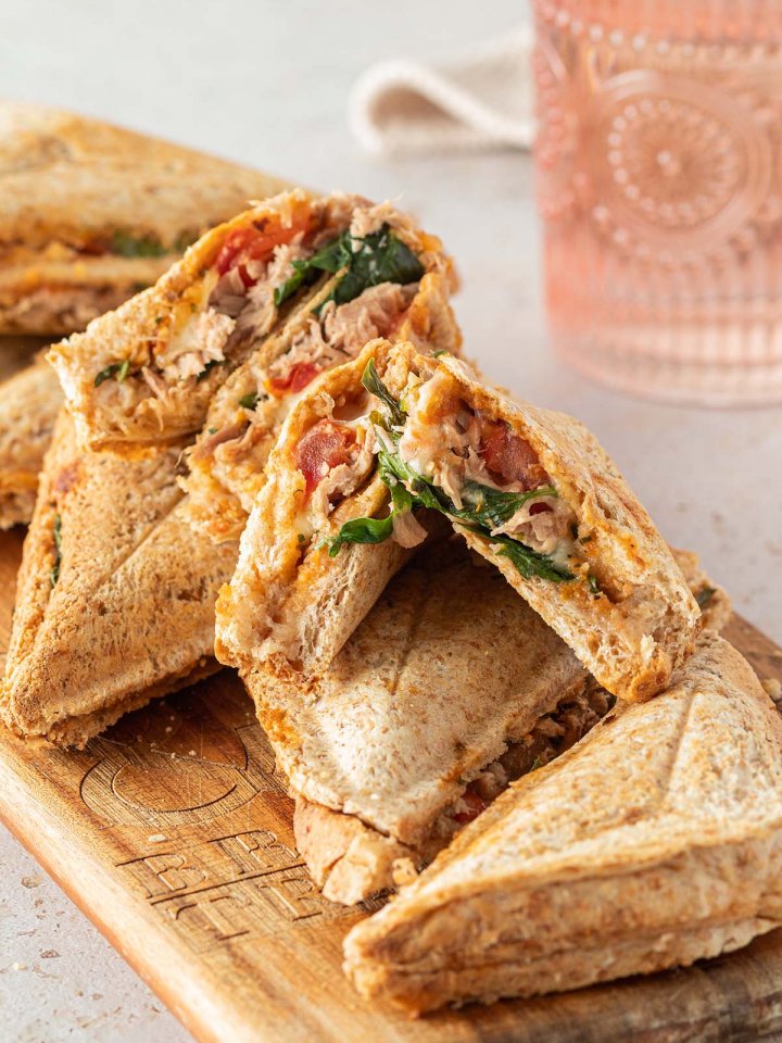Mehrere, warme Thunfisch Sandwiches auf einem Holzbrett, ein Wasserglas im Hintergrund.