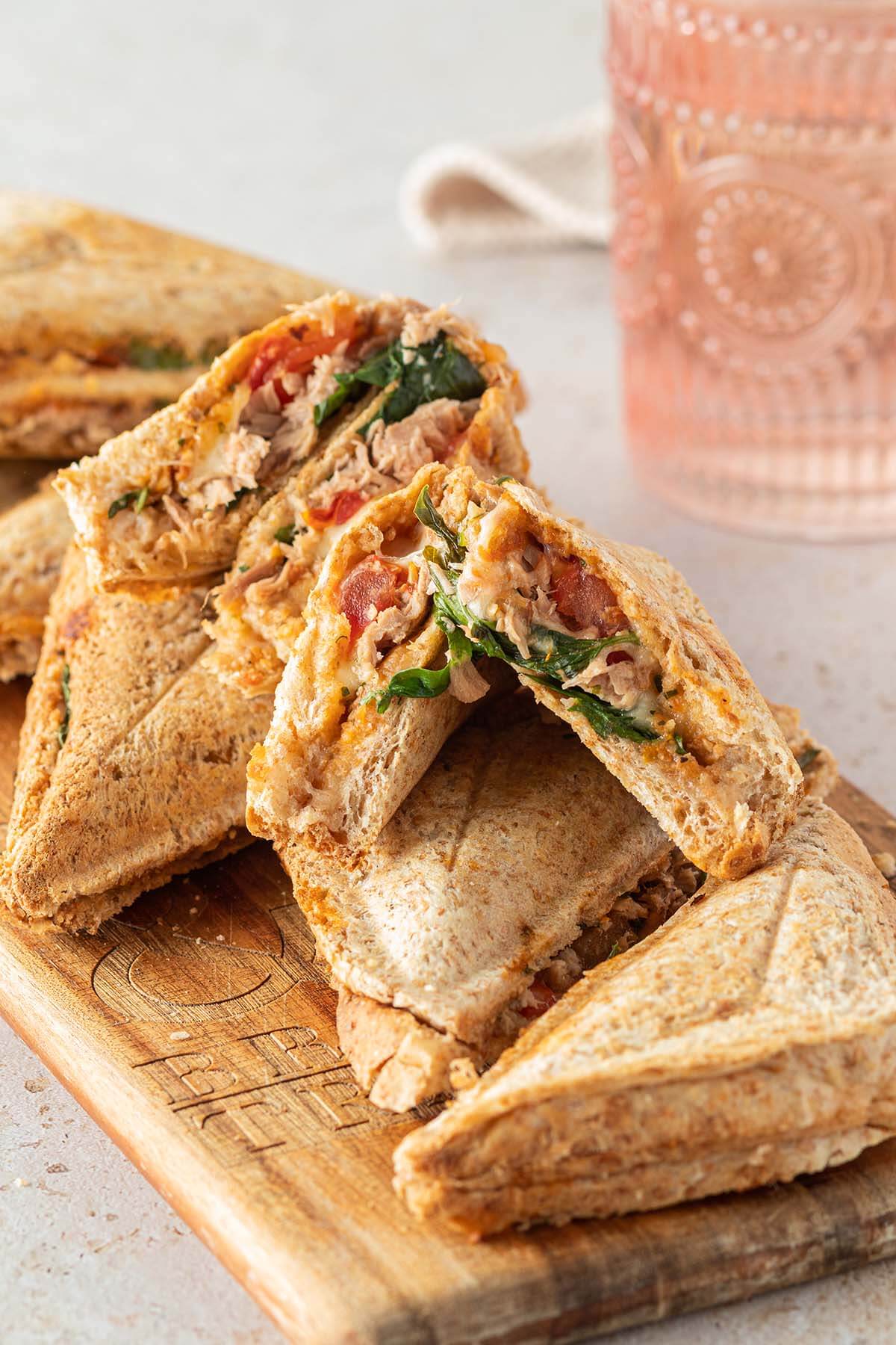 Mehrere, warme Thunfisch Sandwiches auf einem Holzbrett, ein Wasserglas im Hintergrund.