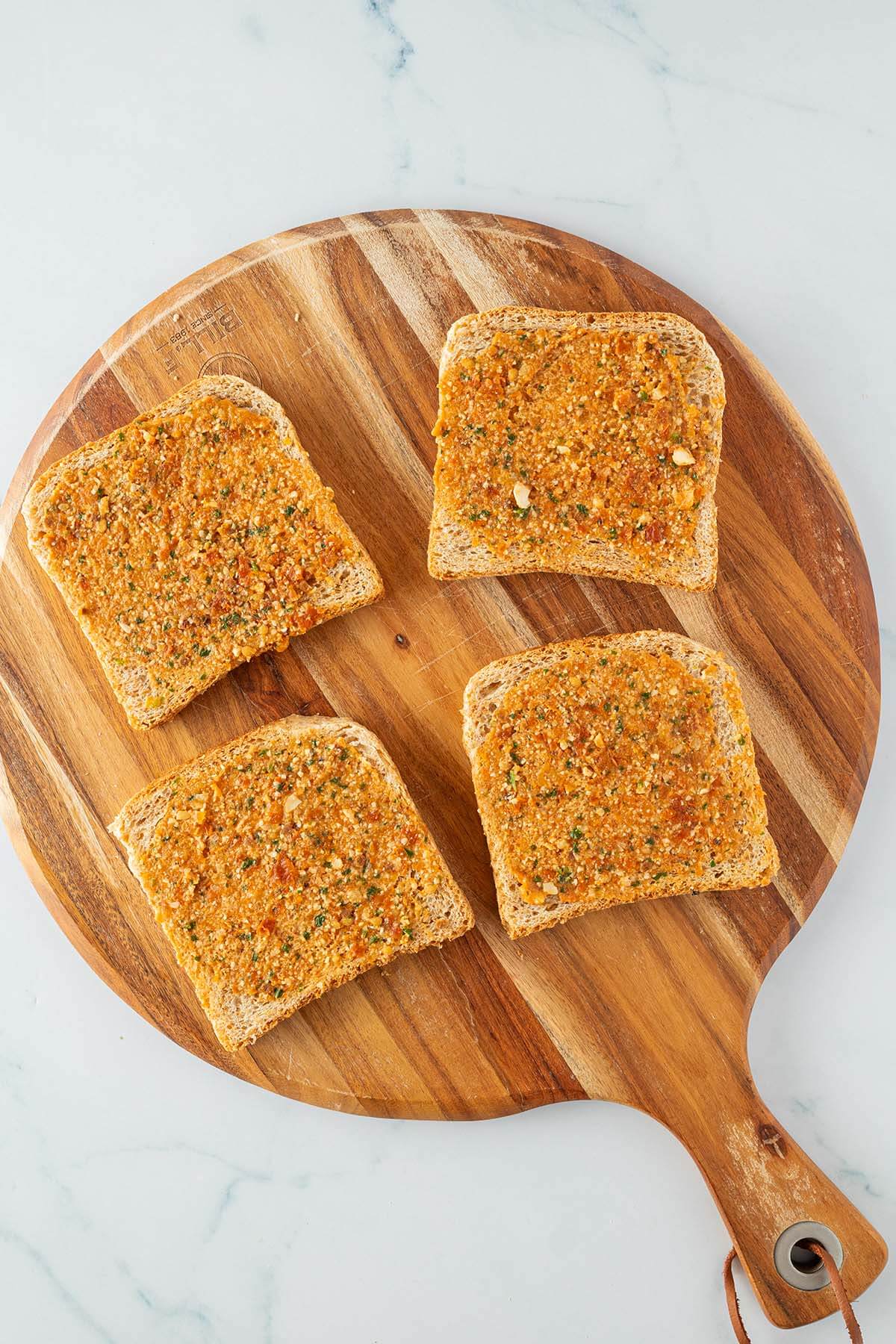Vier Toastscheiben auf einem Holzbrett, die d&uuml;nn mit rotem Pesto bestrichen sind.