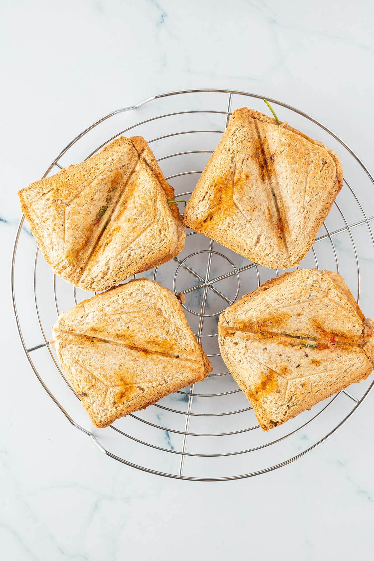 Vier warme, im Sandwichmaker gebratene Sandwiches auf einem Ausk&uuml;hlgitter.