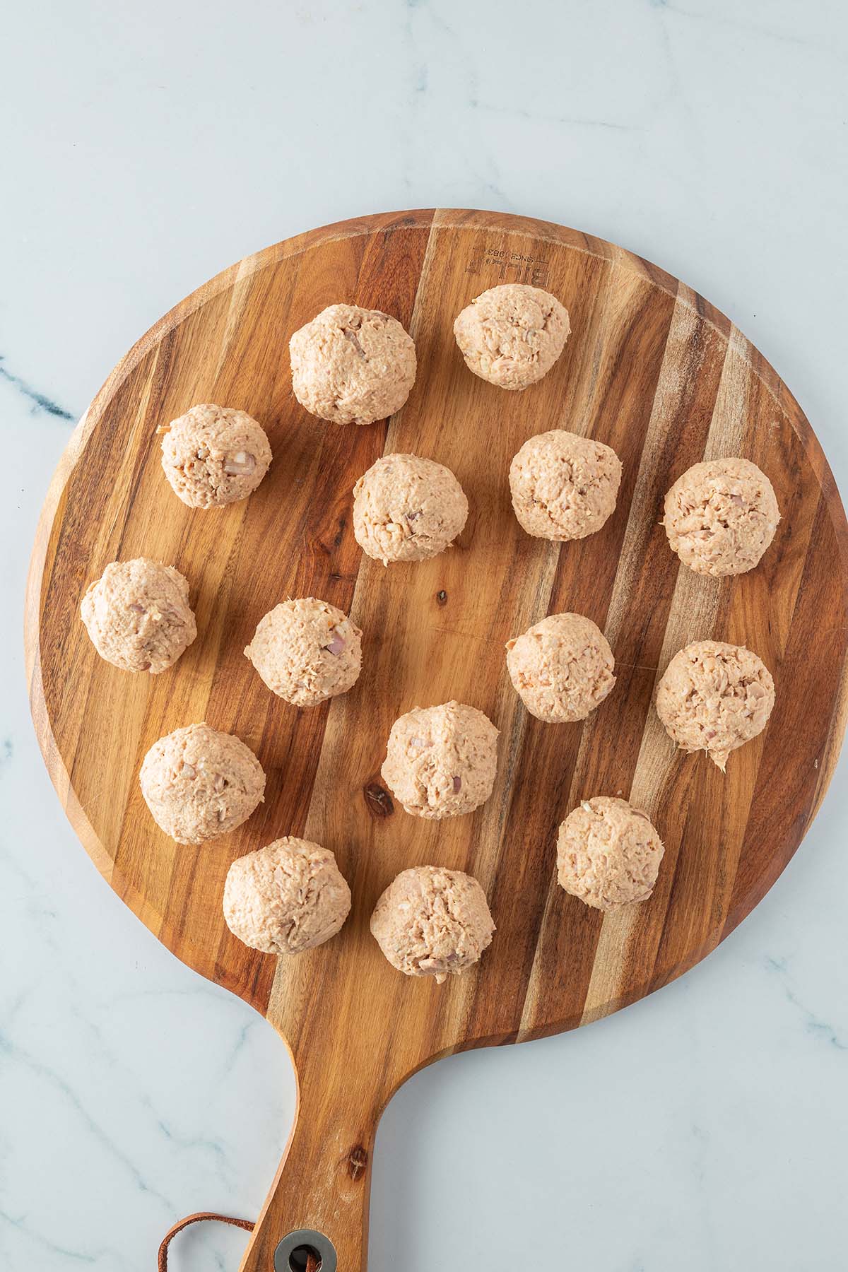Kleine, runde Thunfischb&auml;llchen auf einem Holzbrett.