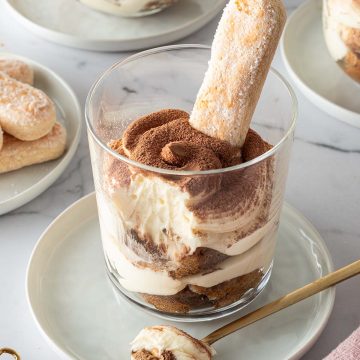 Tiramisu im Glas geschichtet mit L&ouml;ffelbiskuit, im Hintergrund mehr Gl&auml;ser mit Tiramisu und L&ouml;ffelbiskuits.