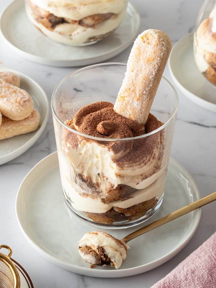 Tiramisu im Glas geschichtet mit L&ouml;ffelbiskuit, im Hintergrund mehr Gl&auml;ser mit Tiramisu und L&ouml;ffelbiskuits.