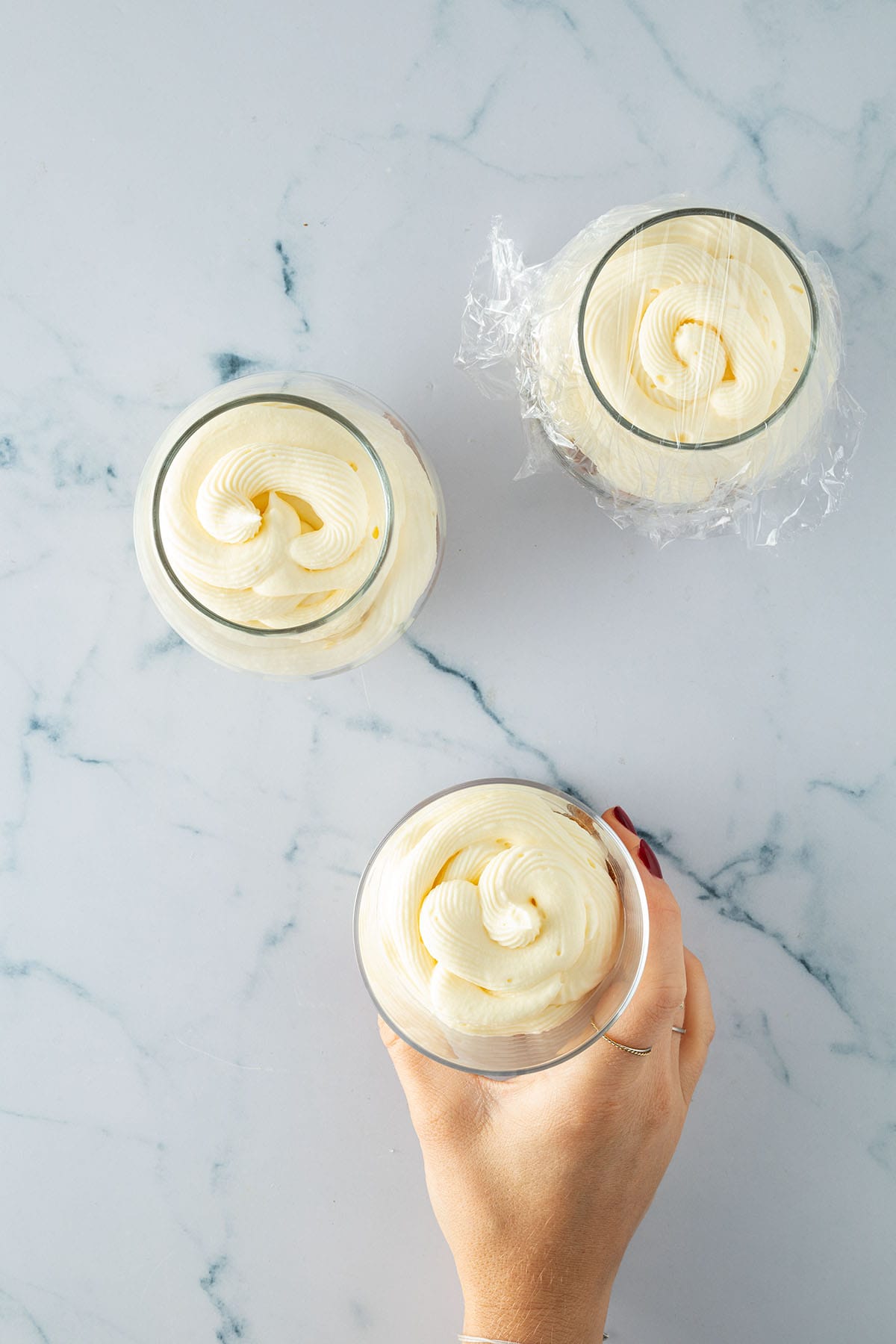 Gl&auml;ser mit frisch aufgespritzter Mascarpone-Creme, eines leicht mit Folie abgedeckt.&ldquo;