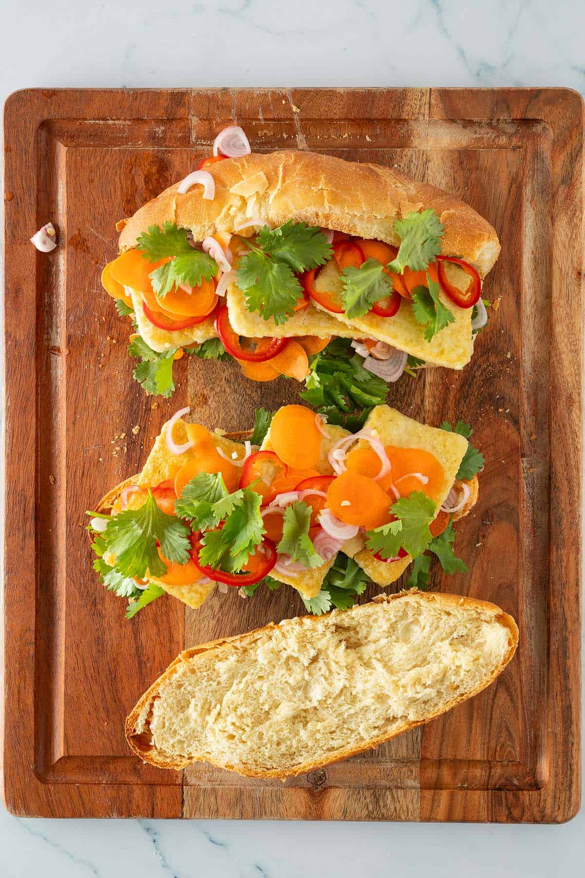 Zwei offene Banh Mi Sandwiches auf Holzbrett, belegt mit Tofu, Karotten, Chili, Schalotten und Koriander.