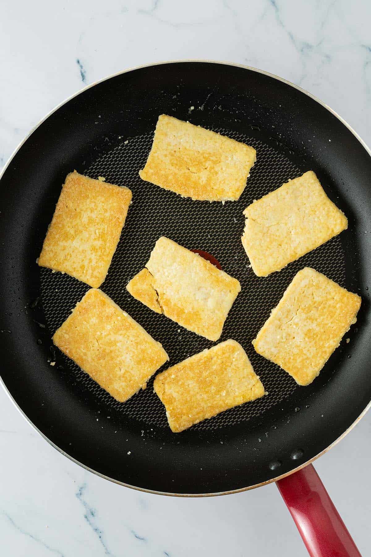 Goldbraun gebratene Tofuscheiben in einer Pfanne.