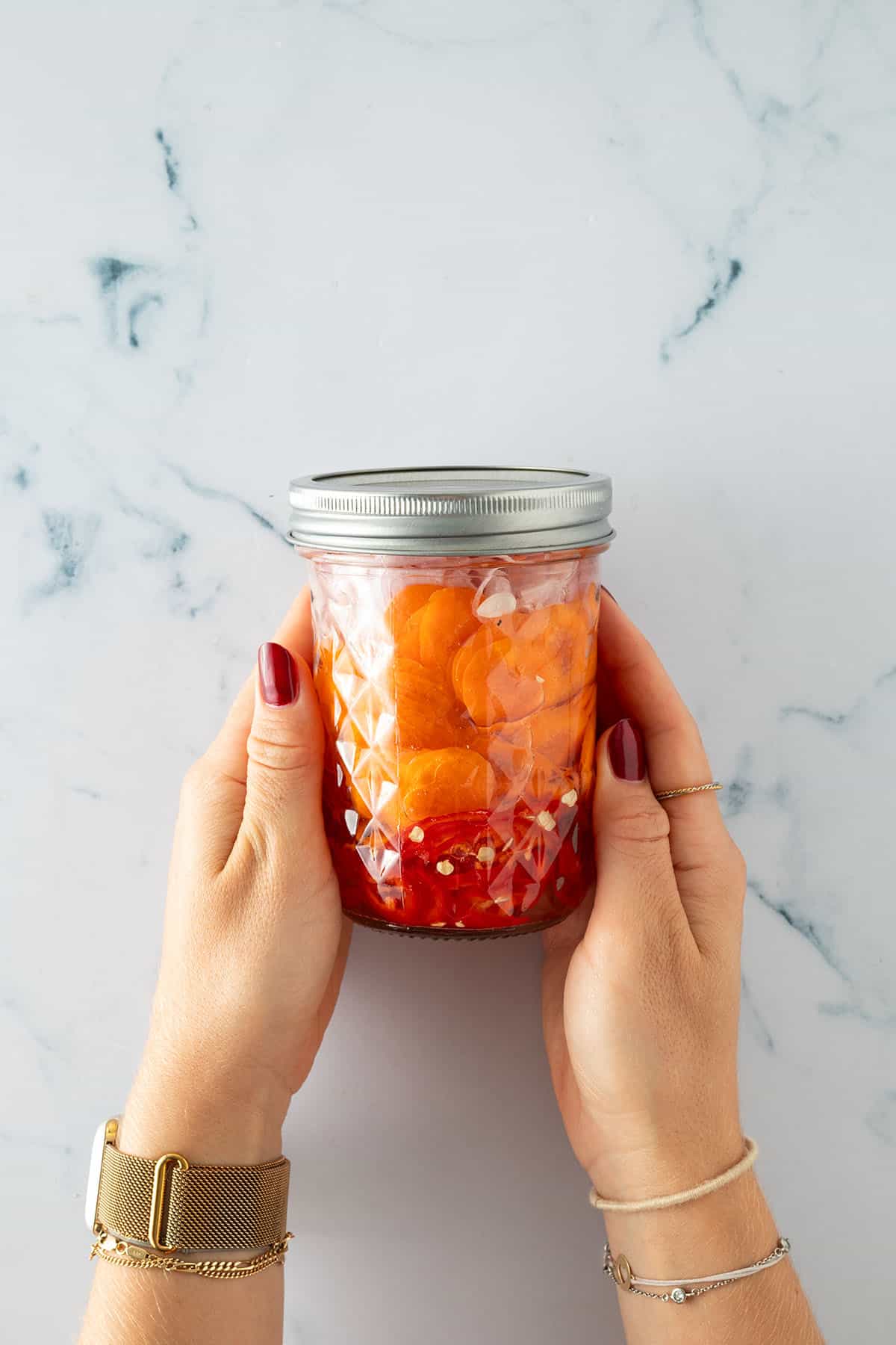 H&auml;nde halten ein Glas mit eingelegten Karotten und Chili in einer Essigfl&uuml;ssigkeit.