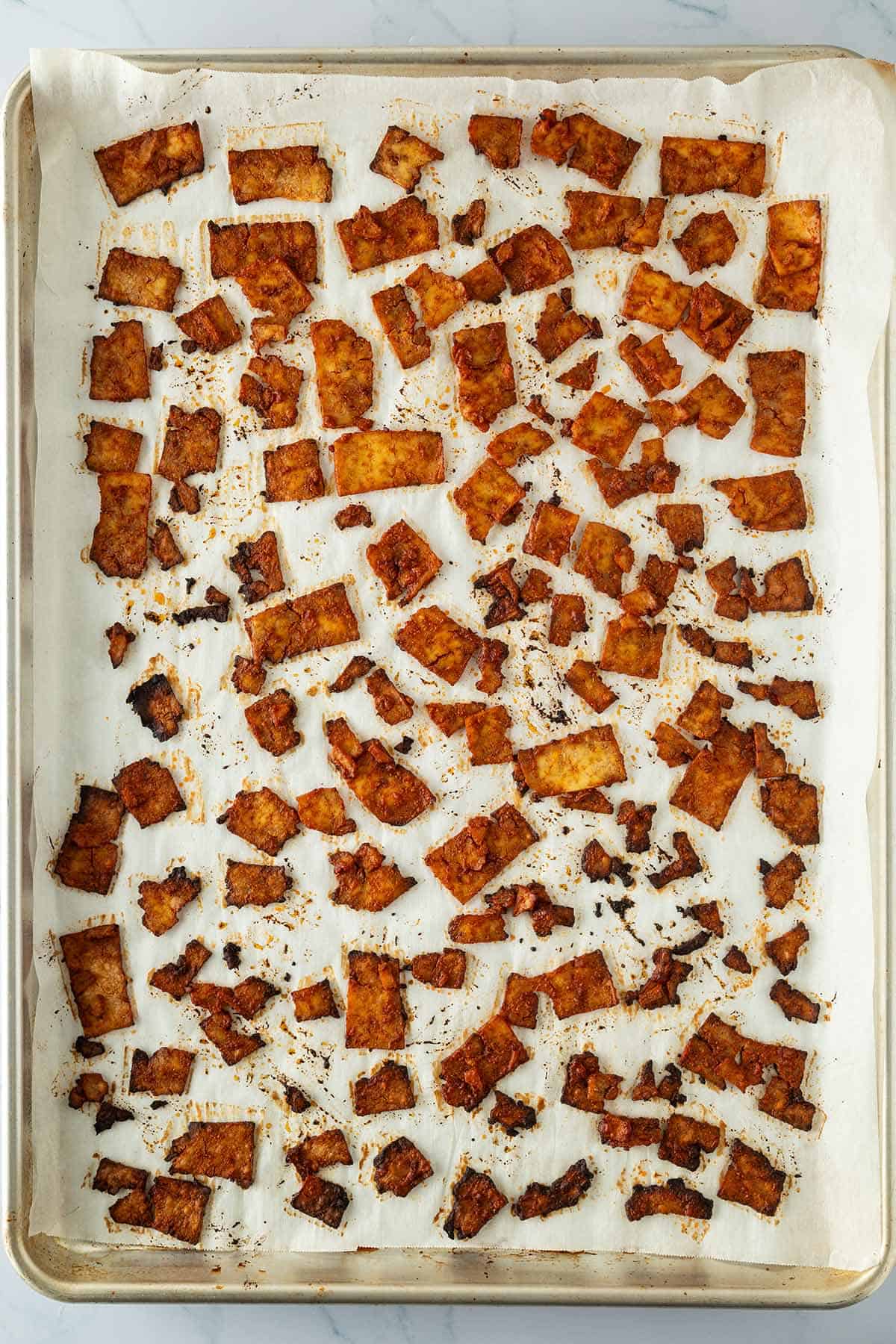 Kleine, d&uuml;nne, marinierte und knusprig gebackene Tofu-Scheiben auf einem Backblech.