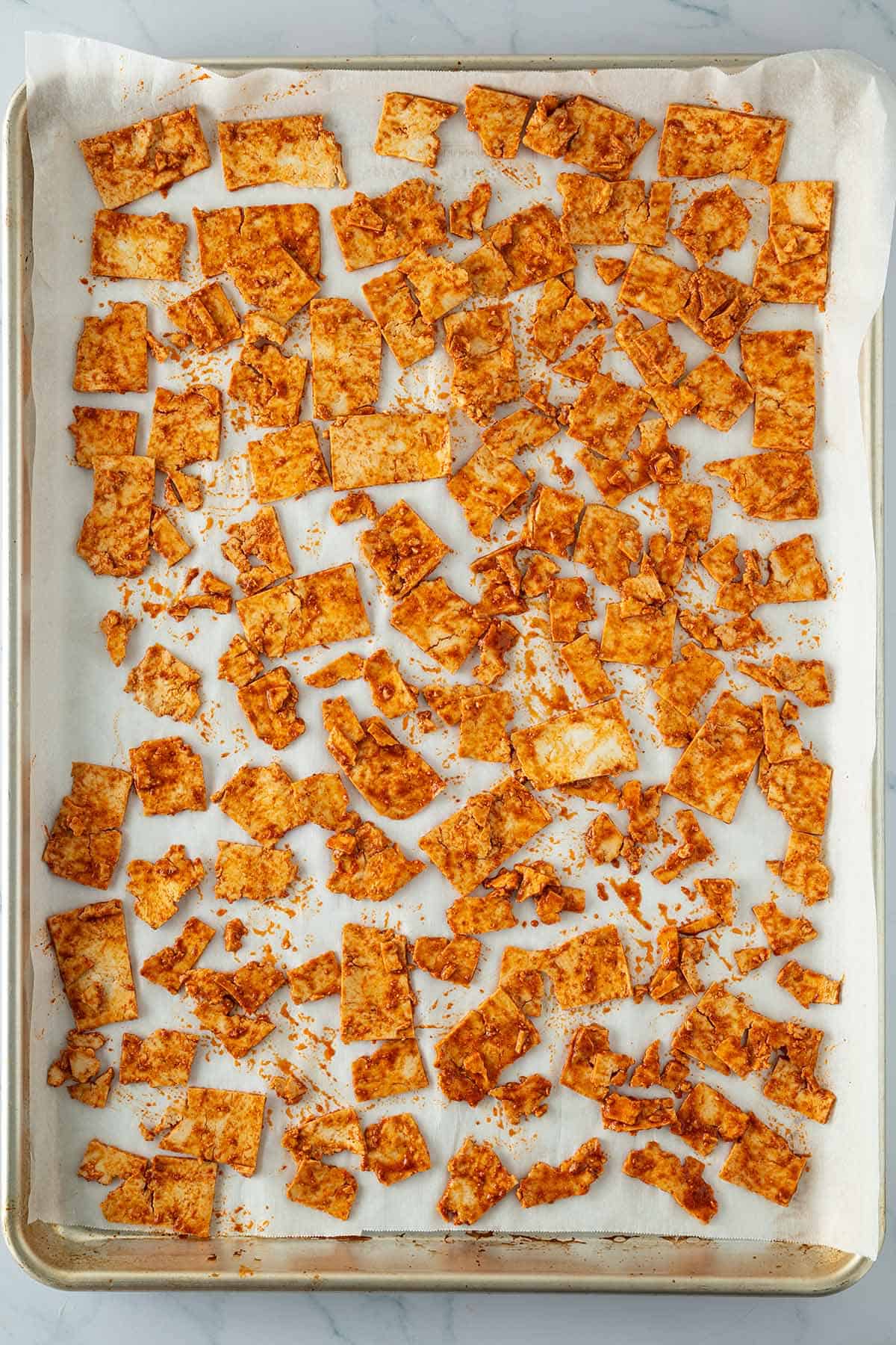 D&uuml;nne, marinierte Tofu-Scheibchen auf einem mit Backpapier ausgelegtem Blech.