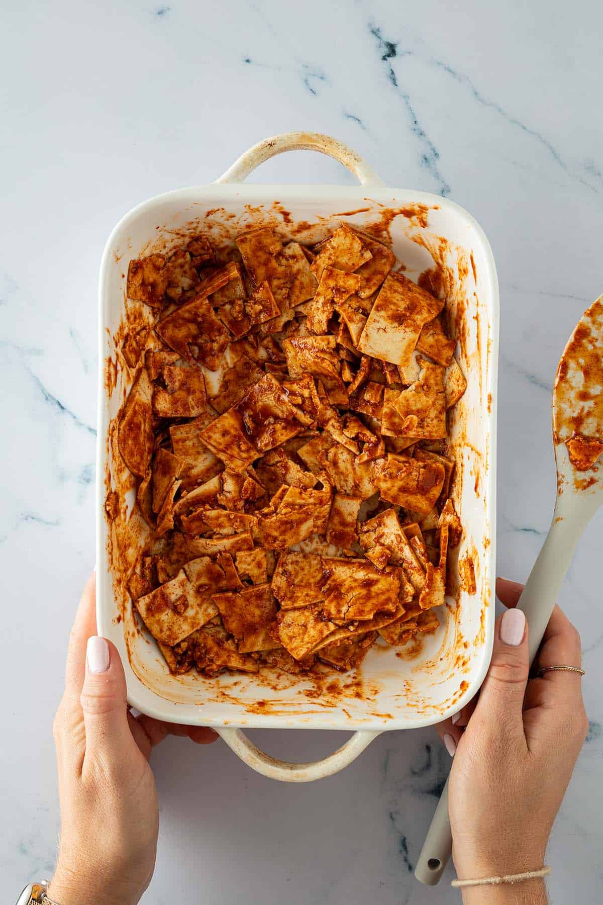 Eine Person h&auml;lt eine Auflaufform in der d&uuml;nne, kleine Tofu-Scheiben mit einer Marinade vermischt wurden.