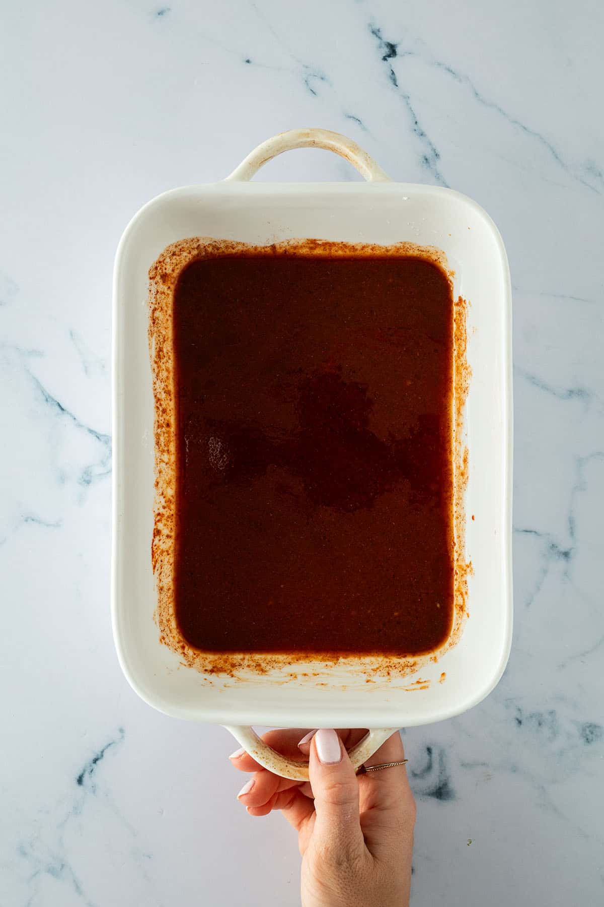 Eine Auflaufform mit einer dunkelroten Marinade wird von jemand in der Hand gehalten.