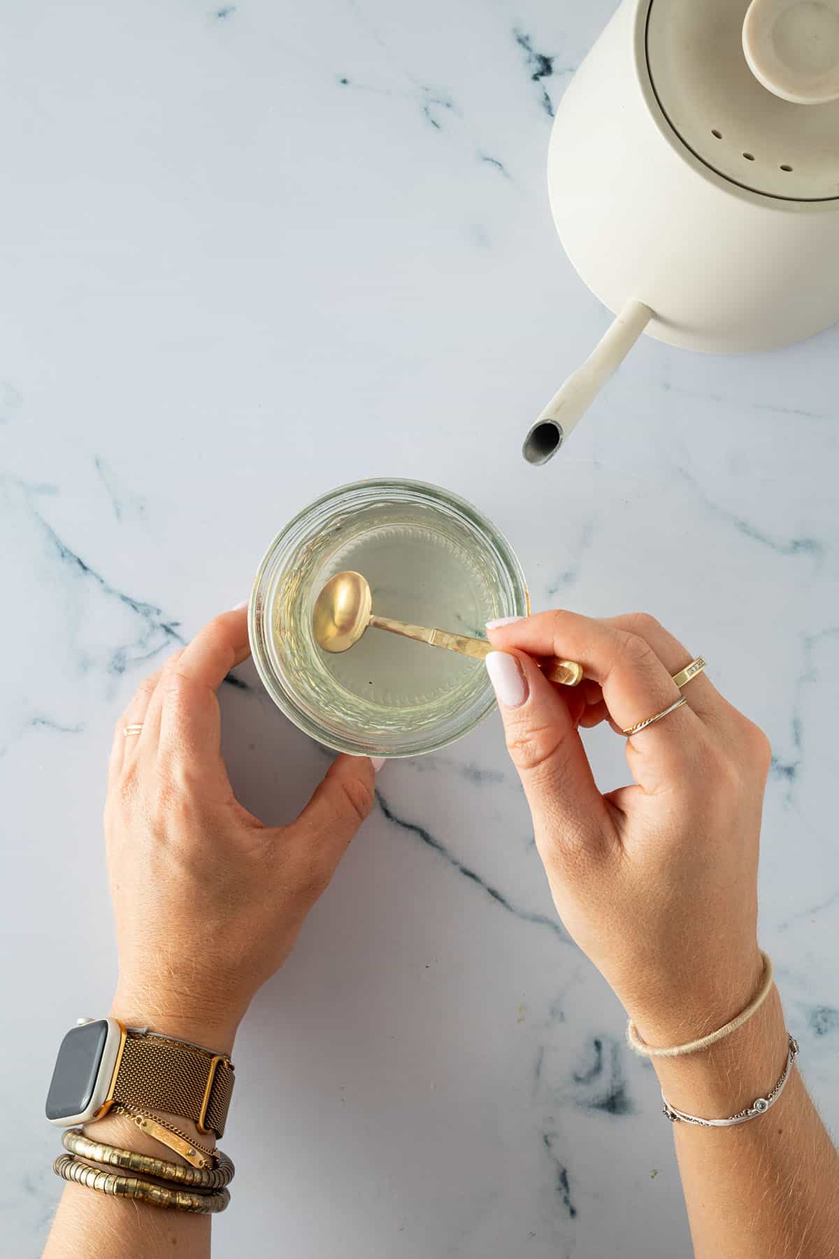 H&auml;nde r&uuml;hren eine klare Pickling-Fl&uuml;ssigkeit in einem Glas mit einem goldenen L&ouml;ffel um.