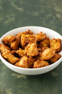 Knusprige, marinierte Tofuw&uuml;rfel aus dem Airfryer in einer wei&szlig;en Sch&uuml;ssel.