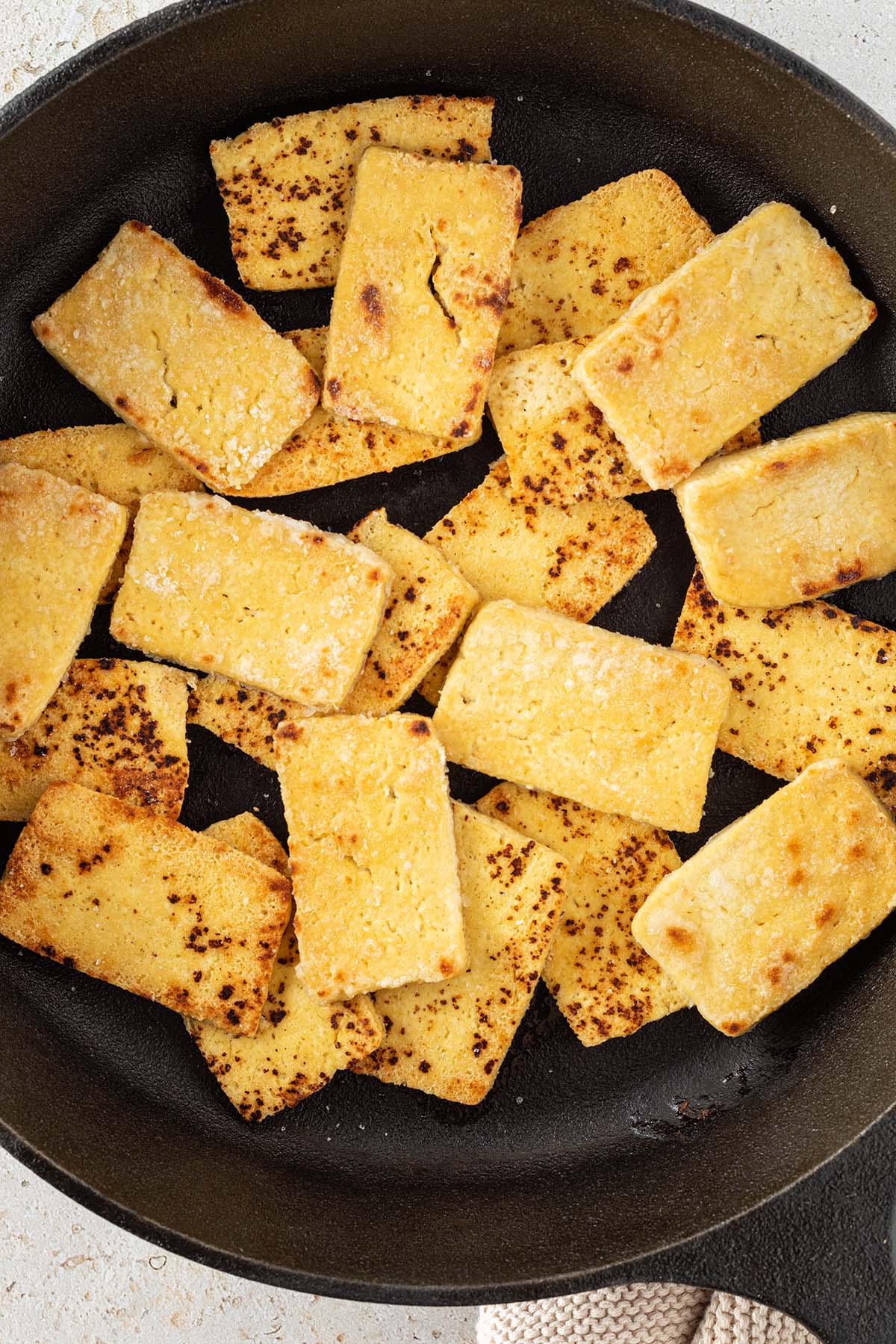 Nahaufnahme von knusprig angebratenen Tofu-Scheiben in einer Gusseisenpfanne.