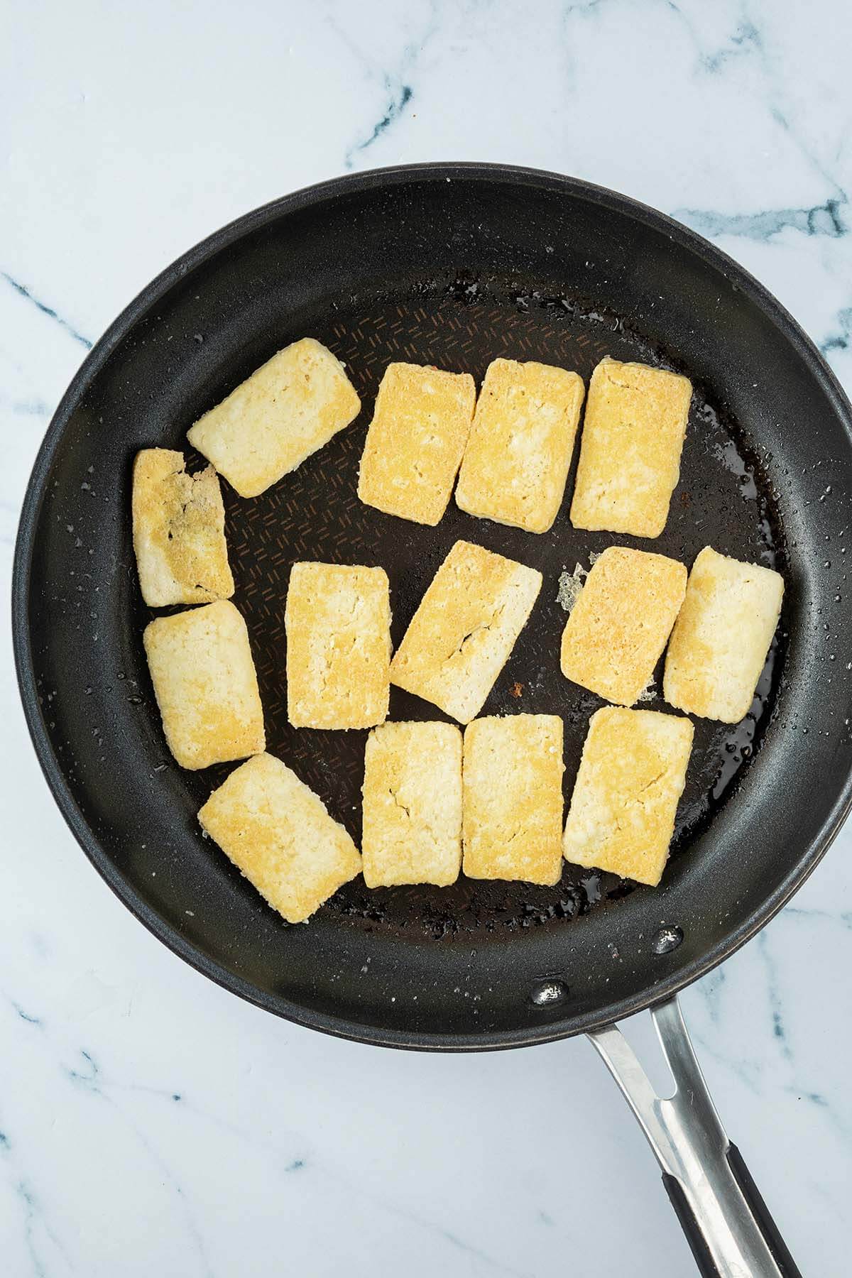 Vogelperspektive auf eine Pfanne mit goldbraunen Tofu-Scheiben darin.
