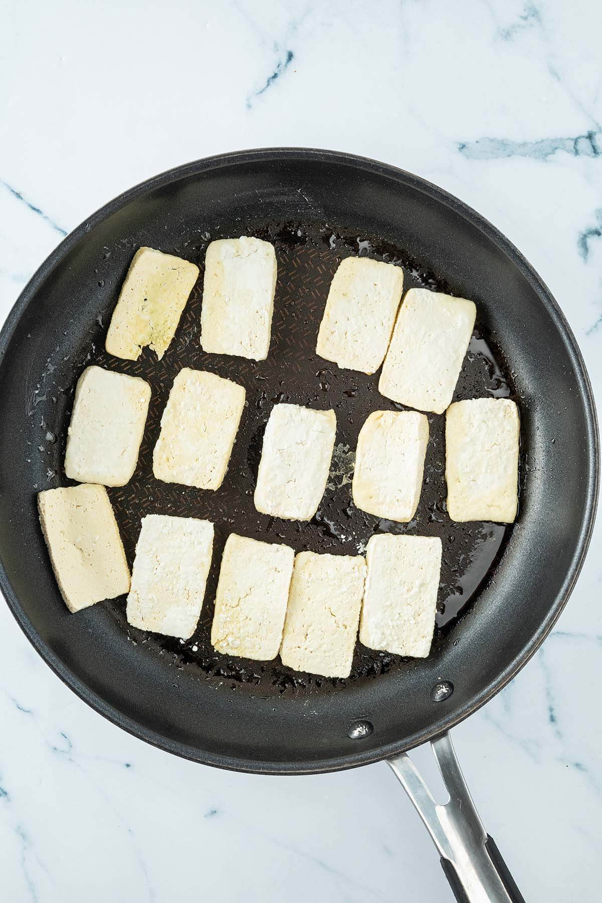 Vogelperspektive auf eine Pfanne in der in Scheiben geschnittener Tofu in etwas &Ouml;l angebraten wird.