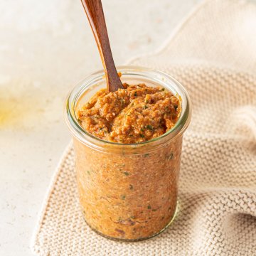 Ein Glas Tomatenpesto und einem kleinen Holzl&ouml;ffel auf beigen Untergrund.