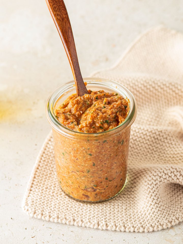 Ein Glas Tomatenpesto und einem kleinen Holzl&ouml;ffel auf beigen Untergrund.