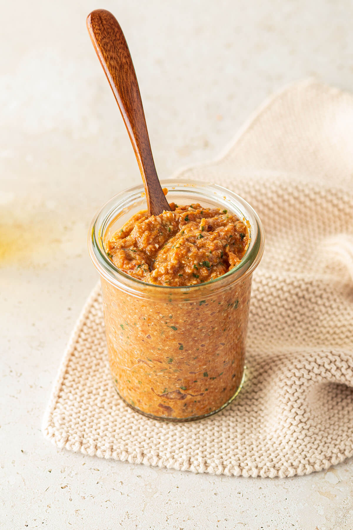 Ein Glas Tomatenpesto und einem kleinen Holzl&ouml;ffel auf beigen Untergrund.
