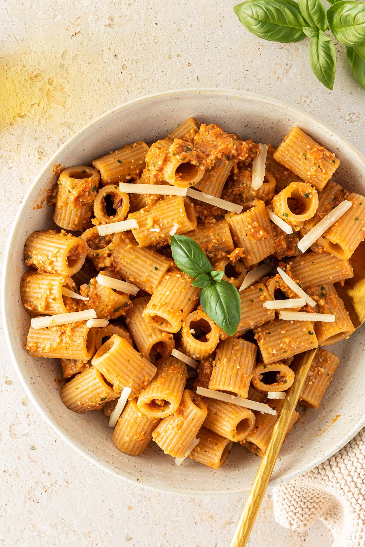 Ein Teller Rigatoni Nudeln mit rotem Pesto, Parmesanhobeln und frischem Basilikum.