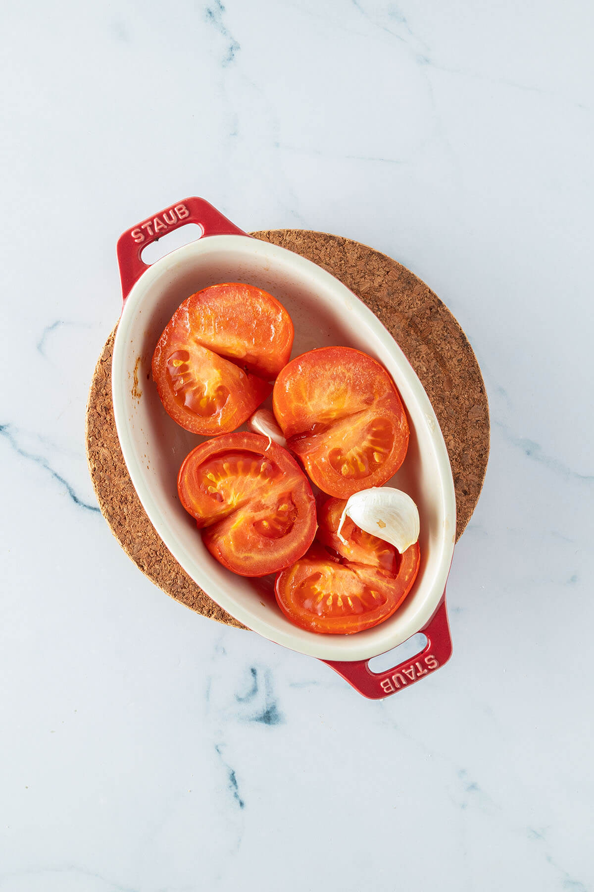 Halbierte Fleischtomaten und zwei Knoblauchzehen in einer Auflaufform, die im Ofen ger&ouml;stet wurden.