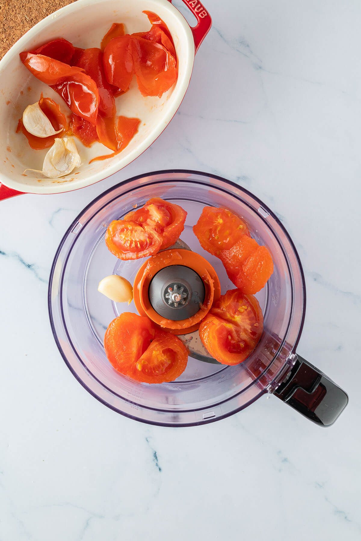 Gesch&auml;lte Tomaten und Knoblauchzehen in einem Mixer, die Auflaufform mit der Tomatenhaut daneben.