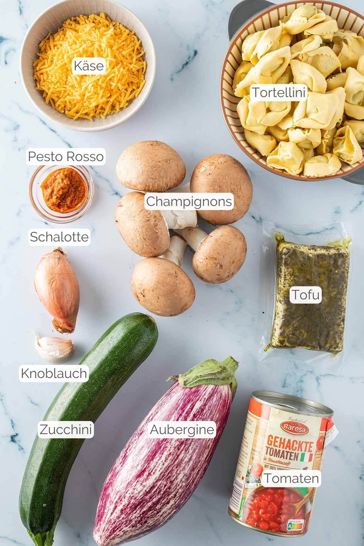 Foto aller Zutaten mit jeweiligen Textbeschriftungen, die f&uuml;r den Tortellini Auflauf ben&ouml;tigt werden.