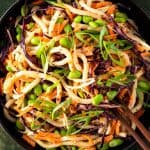 Udon Nudelsalat mit frischem Gem&uuml;se, Edamame Bohnen und einem Erdnussdressing in einem tiefen, schwarzen Teller.