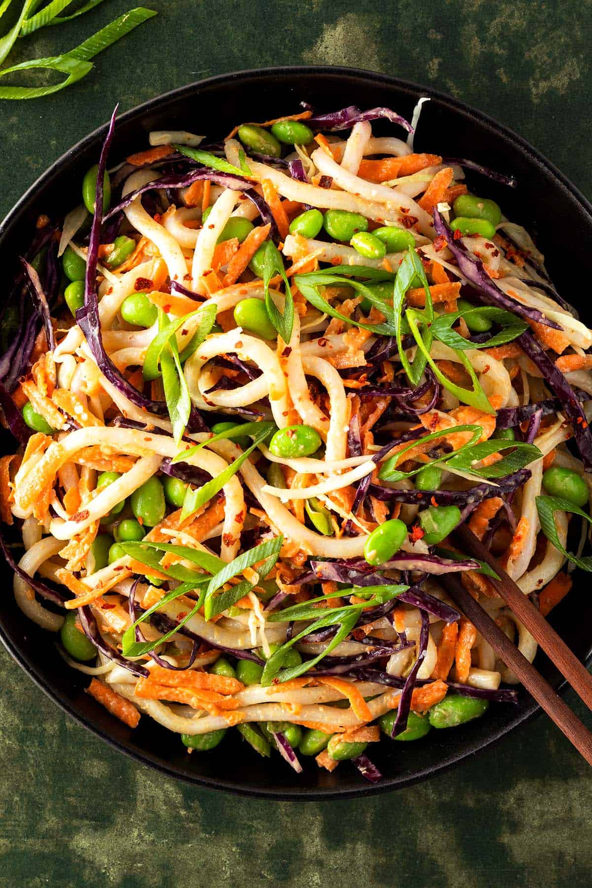 Udon Nudelsalat mit frischem Gem&uuml;se, Edamame Bohnen und einem Erdnussdressing in einem tiefen, schwarzen Teller.
