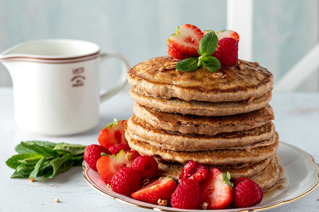 Stapel vegane Pancakes mit Himbeeren und Erdbeeren sowie frischer Minze und Ahornsirup serviert