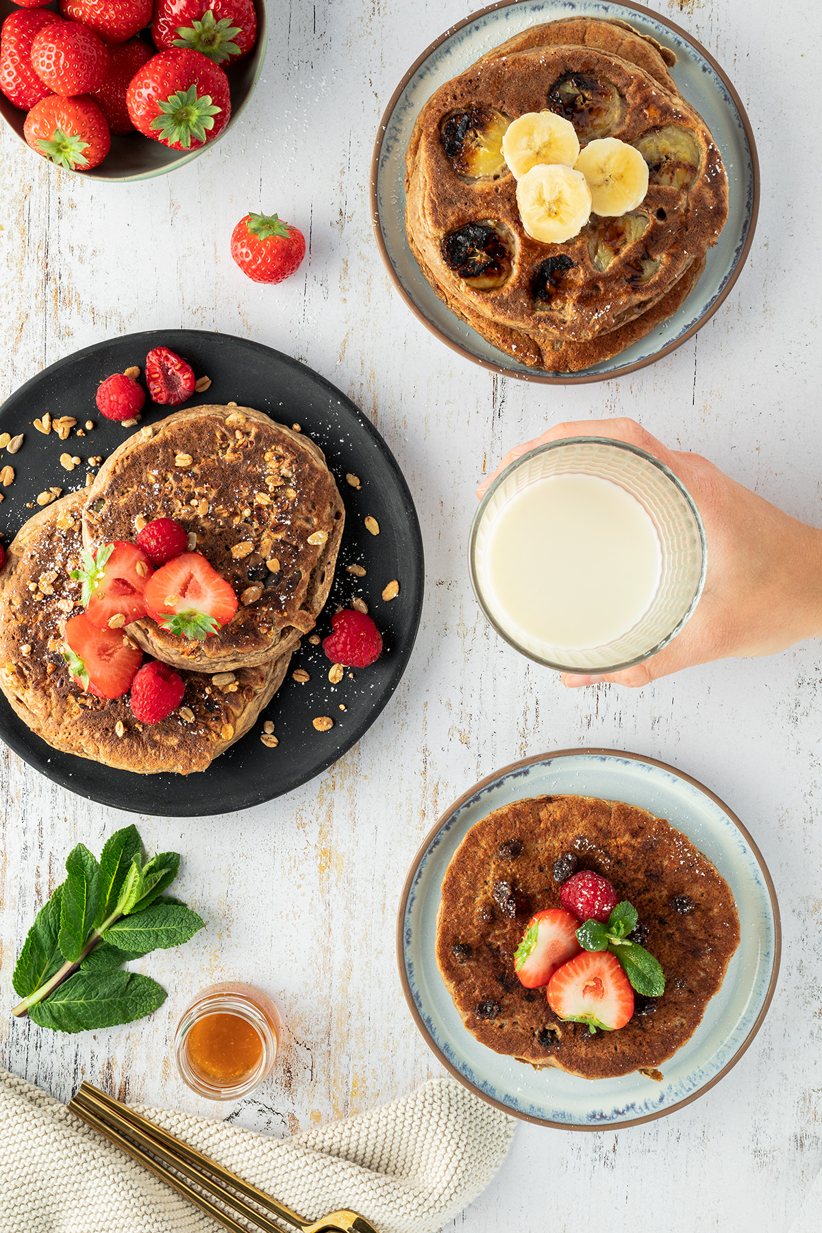 Fr&uuml;hst&uuml;ckstisch mit drei Tellern, darauf die veganen Pancakes mit unterschiedlichen Toppings